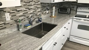 Una cocina con un lavamanos de acero inoxidable, armarios blancos, un microondas y un horno empotrado.