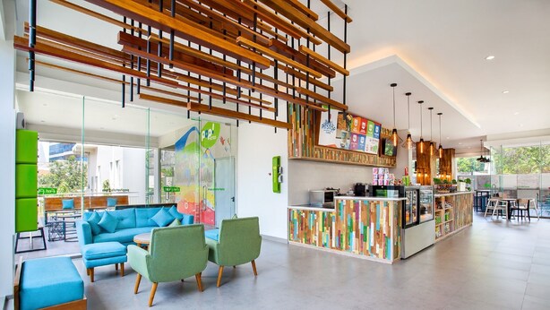 Eine geräumige Lobby mit einem blauen Sofa, grünen Sesseln, einem Holzbalken-Design an der Decke und einem bunten Spielbereich für Kinder.
