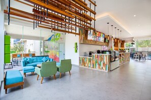 Um hall amplo com um sofá azul, cadeiras verdes, design de teto em madeira e uma área de recreação infantil colorida.