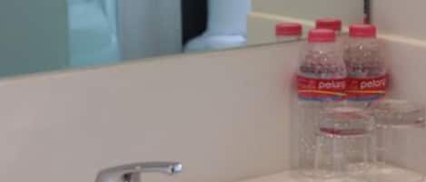 A bathroom with a sink, mirror, and a bottle of water.