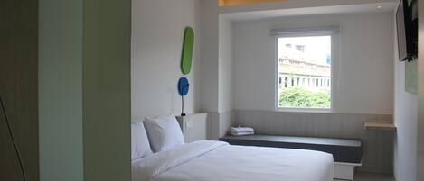 A modern hotel room with a large bed, a bench, a window with a view, and a flat-screen TV mounted on the wall.