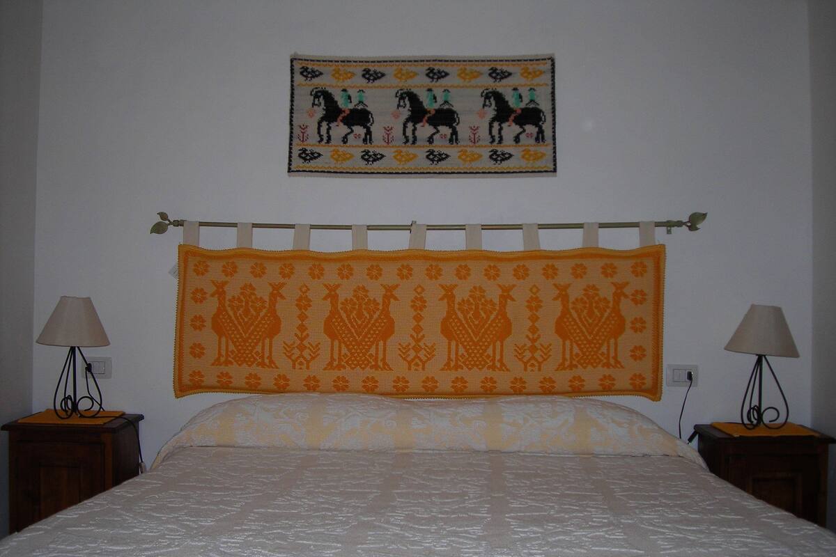 A bedroom with a bed, two nightstands, a wall hanging, and a lamp on each nightstand.