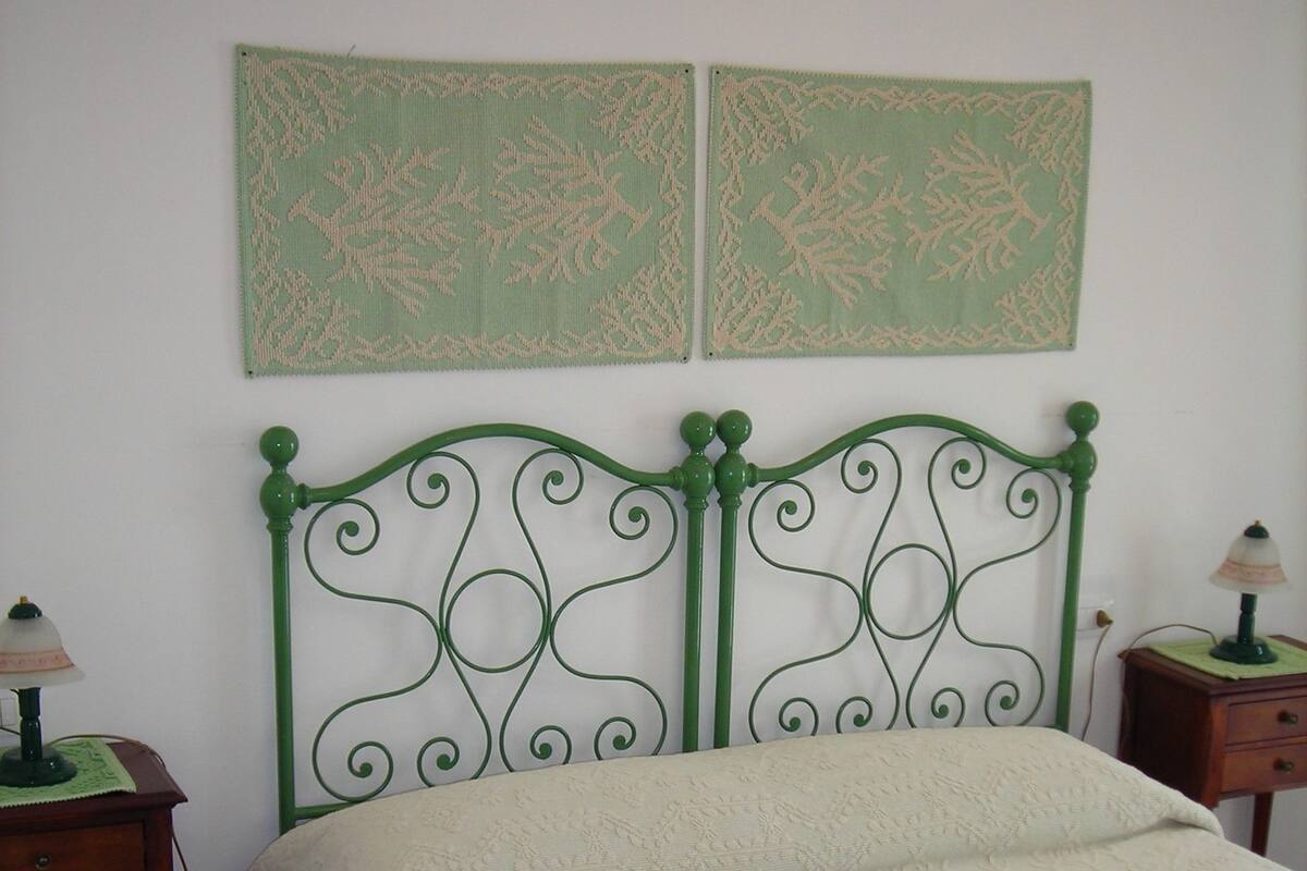 A bedroom with a green metal headboard, a white bedspread, two wall-mounted lamps, and a green rug.