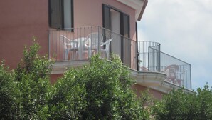 A pink building with a balcony featuring white plastic chairs and a metal railing. - Bed and Breakfast Dessole (Olbia)