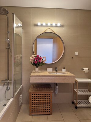 Ein Badezimmer mit Dusche, Waschbecken, Spiegel, Waschtisch und einem kleinen hölzernen Hocker.