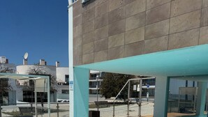 Ein Schwimmbecken mit Fliesen umrandet, einem überdachten Sitzbereich und Blick auf Gebäude im Hintergrund.