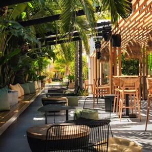 An outdoor seating area with tables and chairs, surrounded by lush greenery and a wooden pergola. - Danaides Hotel (Hersonissos)