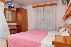 Un dormitorio con una cama, un armario de madera, un televisor y una ventana con cortinas traslúcidas.