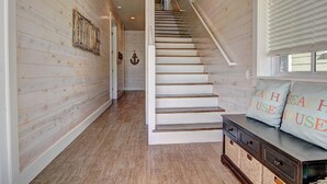 Un intérieur en bois avec un escalier, une décoration murale en forme d’ancre et un banc agrémenté de coussins.