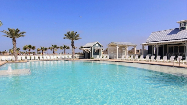 A clear blue pool with lounge chairs and palm trees. - Cinnamon Shore- Sea Change 115 FI (Port Aransas)