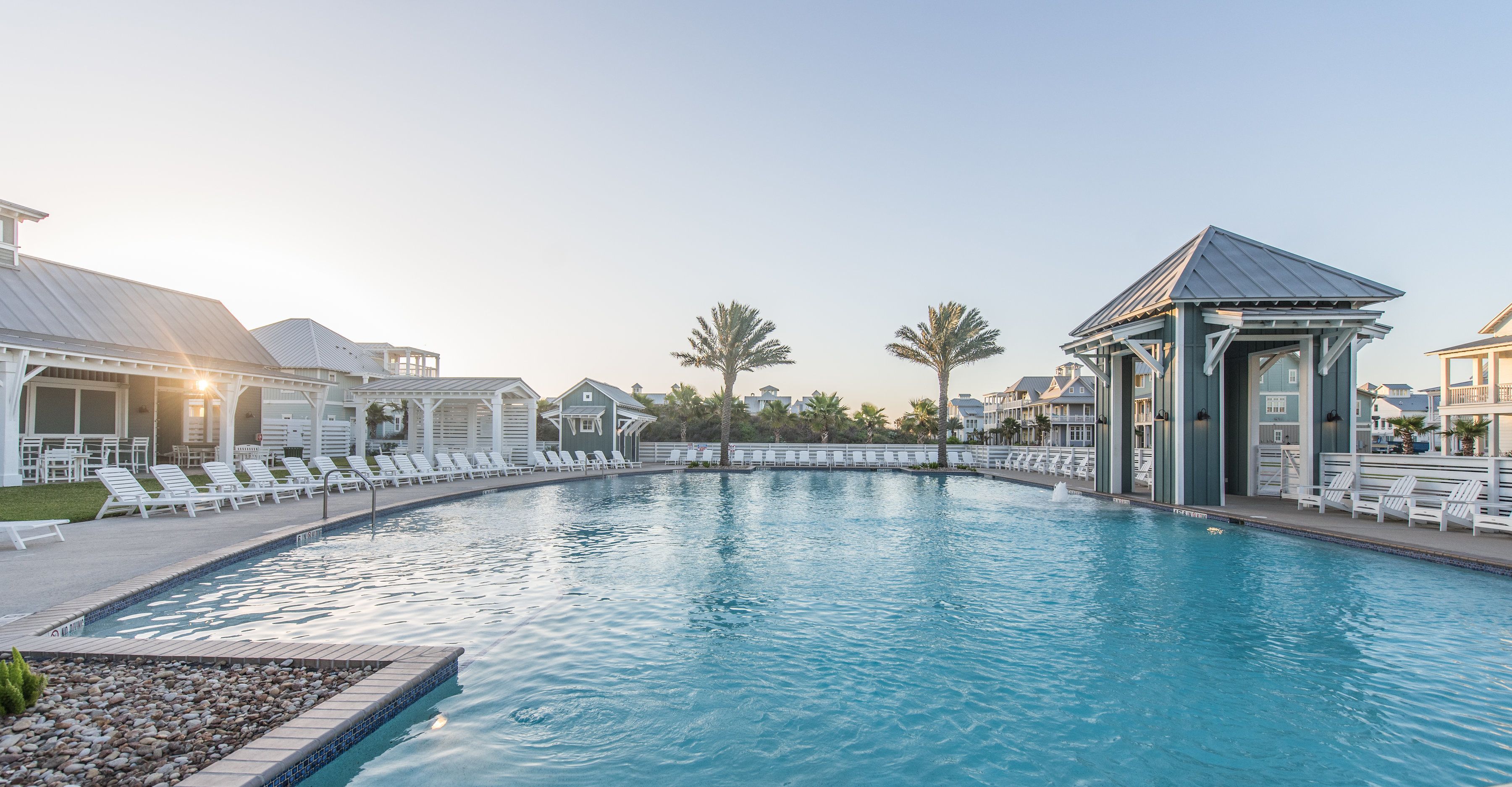 A swimming pool with lounge chairs and a gazebo, surrounded by buildings and palm trees.