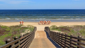 A wooden boardwalk leading to beach umbrellas and lounge chairs on a sandy beach with the ocean in the background. - Cinnamon Shore- Sea Change 115 FI (Port Aransas)