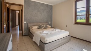 A bedroom with a bed, a window, and a door leading to another room.