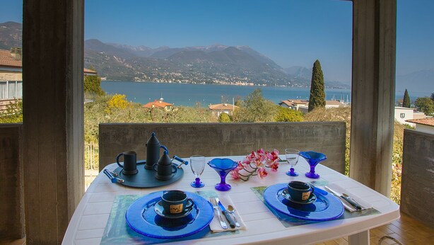 A table set for two with a scenic lake view, a mountain backdrop, and a clear sky.