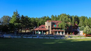A large building with multiple levels and a red roof, surrounded by a white picket fence and trees. - Natyral Razma Resort (Shkrel)