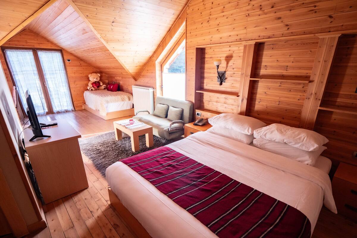A cozy wooden cabin bedroom with a large bed, a desk, a chair, and a TV.
