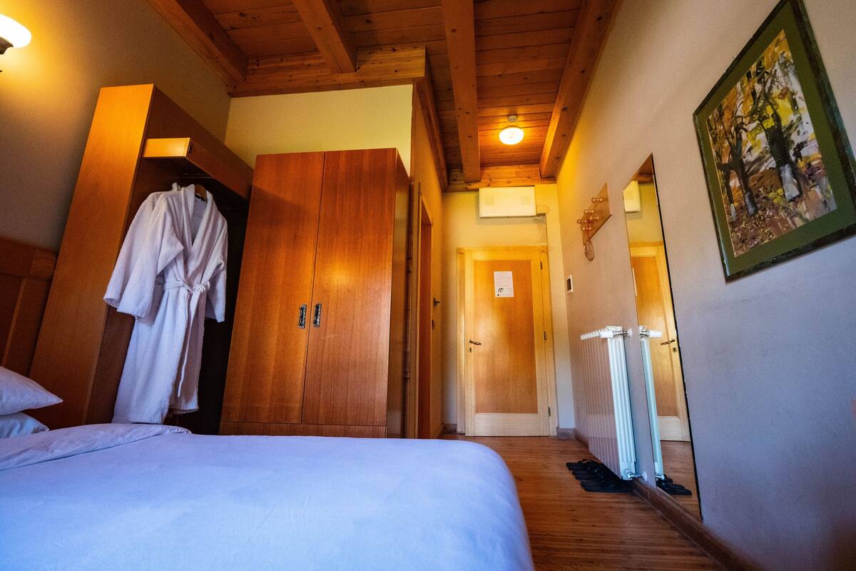 A hotel room with a wooden ceiling, a bed with white bedding, a wooden wardrobe, and a painting on the wall.
