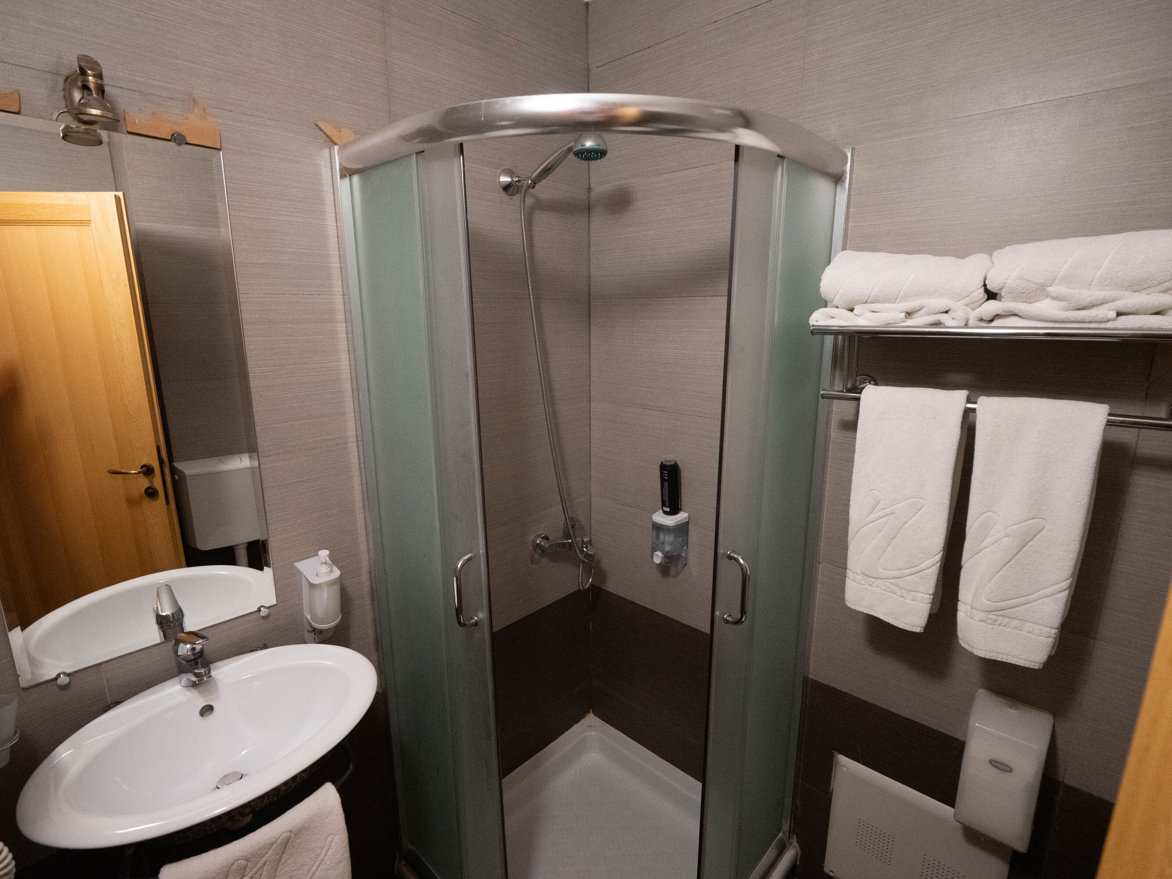 A modern bathroom with a glass-enclosed shower, a sink, and a towel rack with multiple towels.