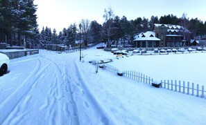 A snow-covered road with parked cars and a building with a snow-covered roof.