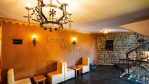 A lobby with a chandelier, a sign reading "NATYRAL RAZMA RESORT", and a stone wall. There are two sofas and a small table. - Natyral Razma Resort (Shkrel)