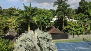 A tennis court surrounded by lush greenery and palm trees. - Gems at CrystalCove (Ocho Rios)