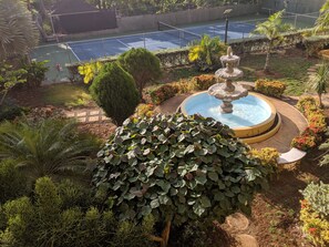 Un court de tennis entouré d’une végétation luxuriante et agrémenté d’une fontaine centrale.