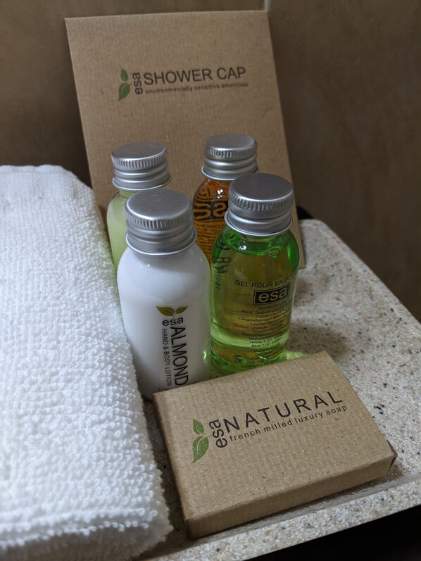 A set of toiletries including a shower cap, almond lotion, and a bottle of gel pour la bed.