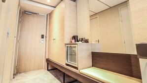 A modern hotel room with a wooden wardrobe, a bench, a small refrigerator, and a mirror. - Arena Hotel La Defense (Nanterre)