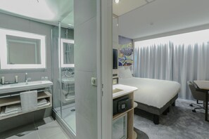 A modern hotel room with a glass-enclosed shower, a large bed, a desk, and a television. - Arena Hotel La Defense (Nanterre)