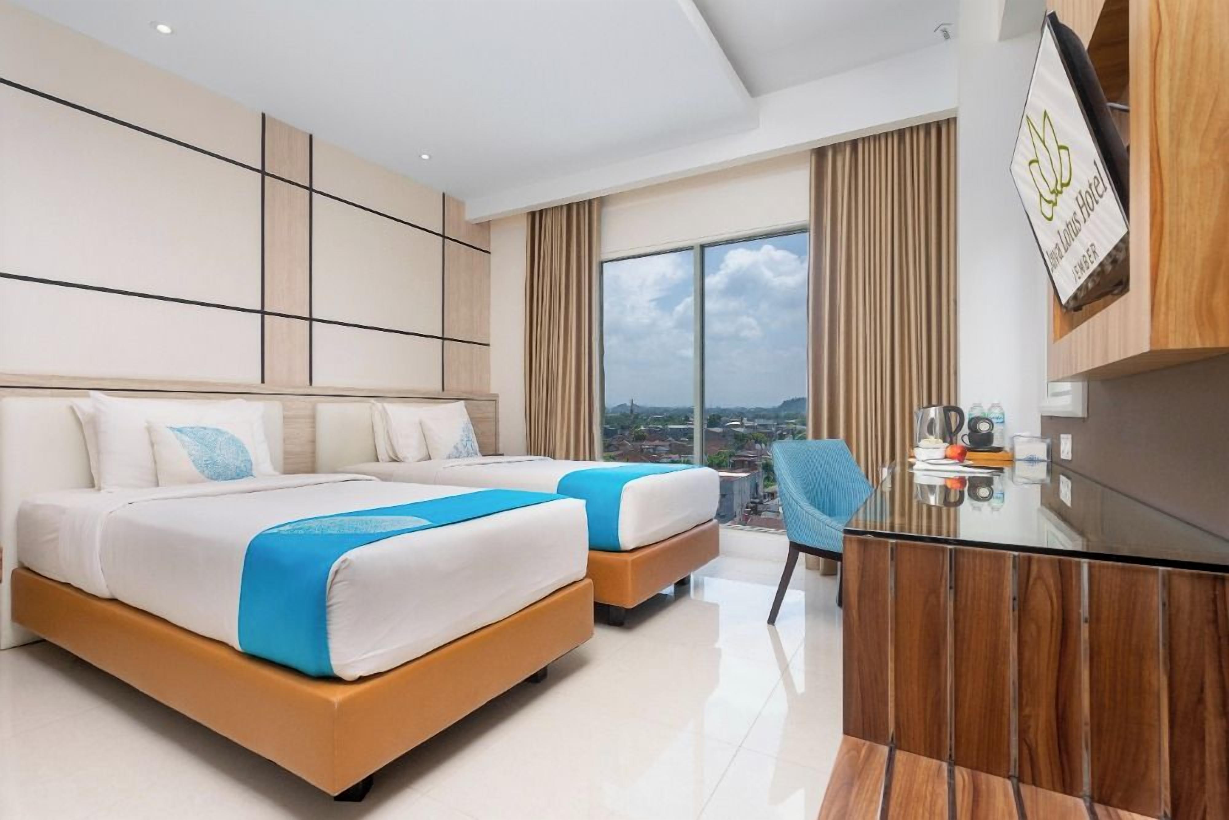 A modern hotel room with two beds, a desk, and a view of the city.