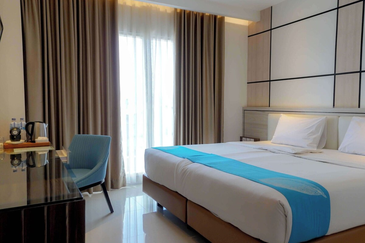 Une chambre d’hôtel avec un grand lit, un bureau avec une chaise et une vue sur l’extérieur par la fenêtre.