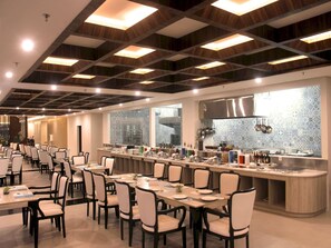 A modern restaurant with a long counter, multiple dining tables, and chairs. - Dafam Lotus Jember Hotel (Jember)