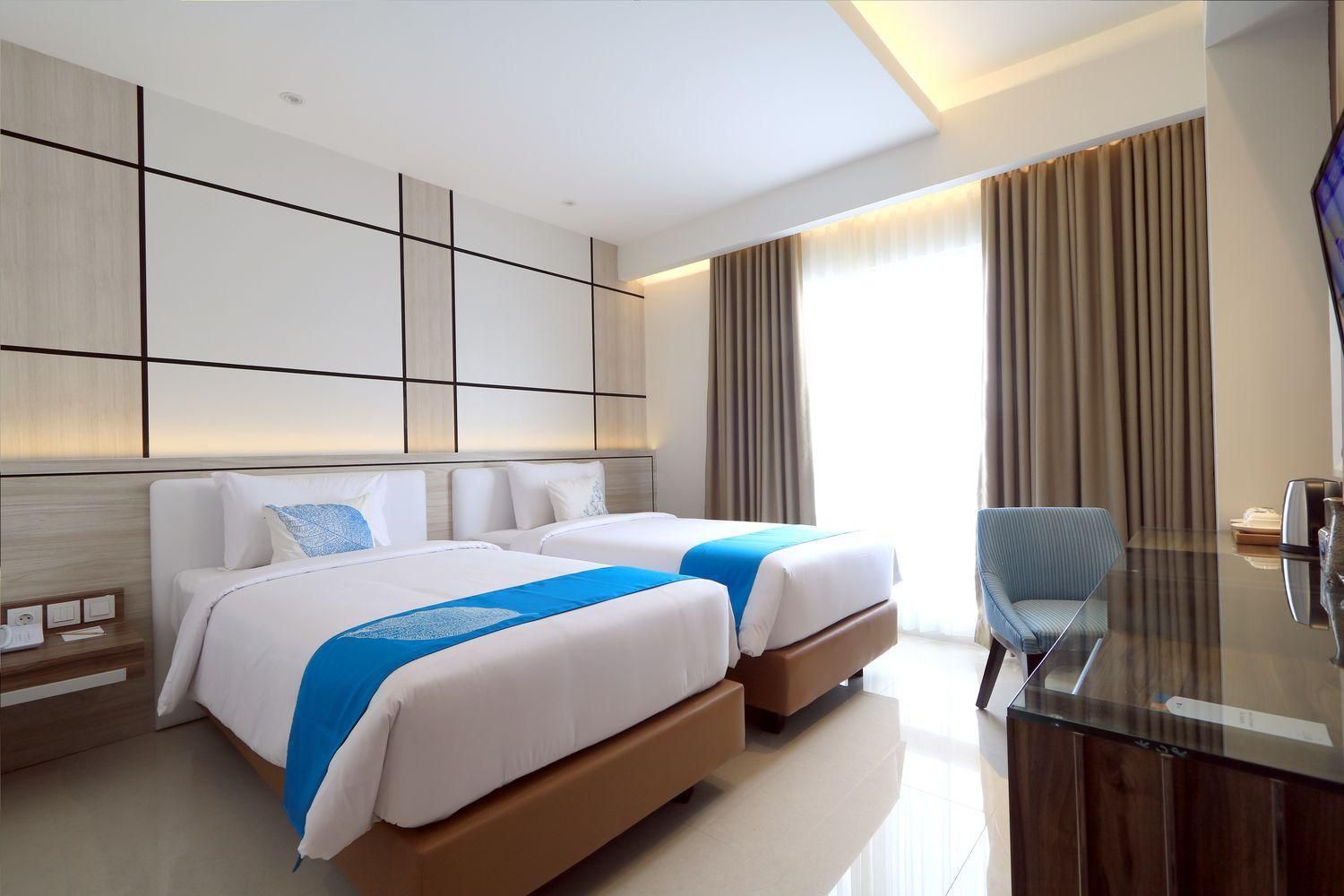 A hotel room with two beds, a desk, and a chair.