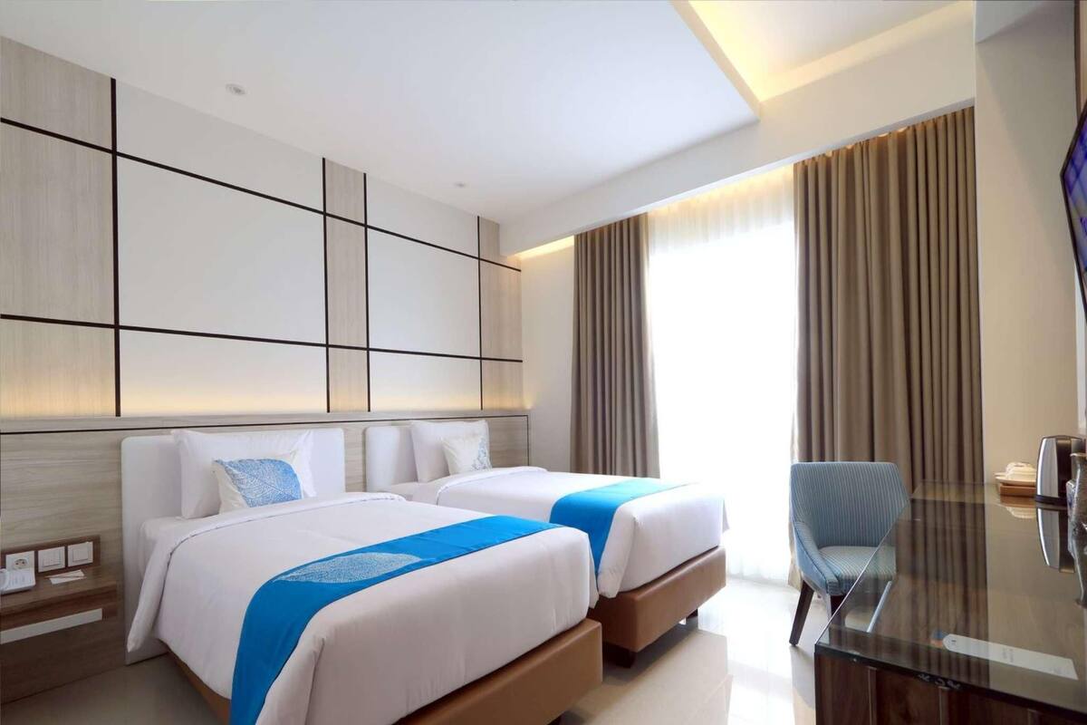 A hotel room with two beds, a desk, and a TV.