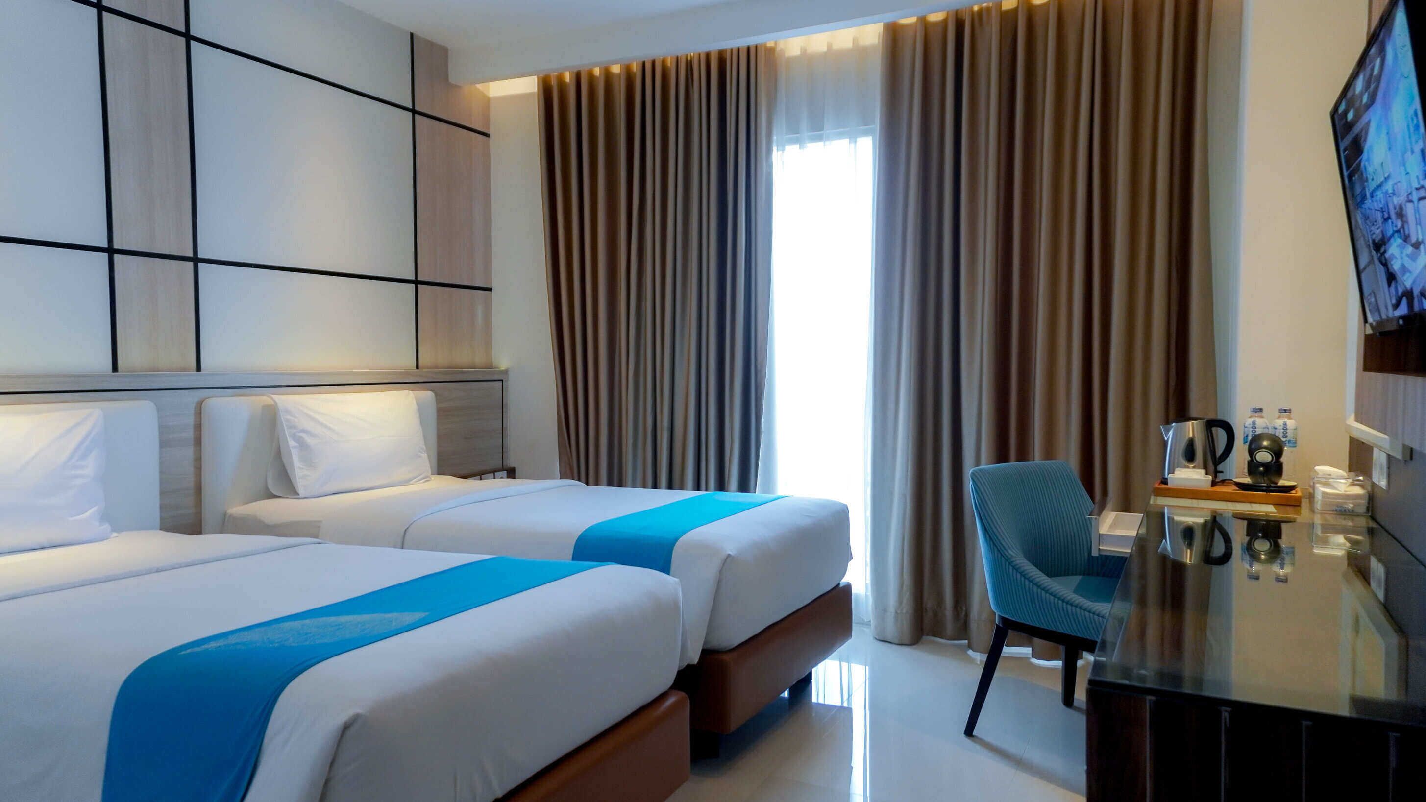 Quarto de hotel com duas camas, uma televisão, uma mesa com cafeteira e uma cadeira.