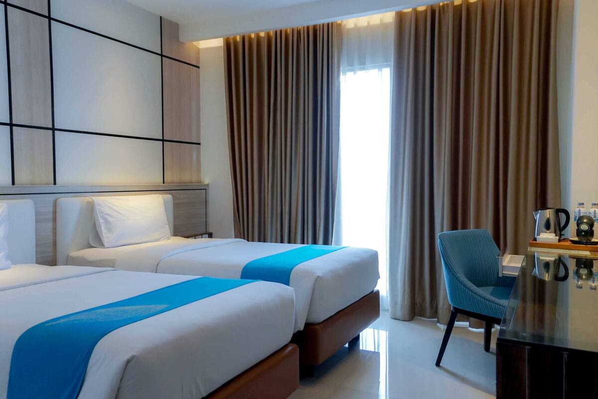 A hotel room with two beds, a TV, a desk with a coffee maker, and a chair.