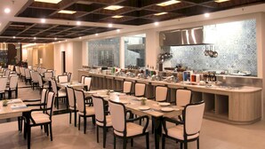 Un comedor amplio con múltiples mesas y sillas, una barra larga con equipo de cocina, y un diseño de techo moderno.