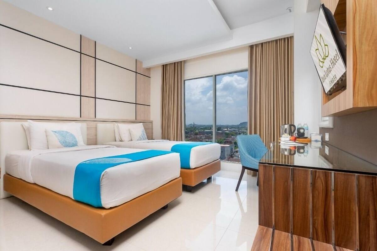 A modern hotel room with two beds, a desk, and a view of the city.