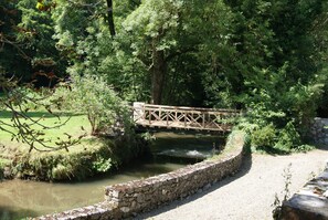 A stone bridge over a calm river, surrounded by lush greenery and trees.
