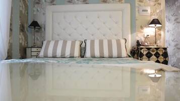 Un dormitorio con cabecera capitonada, almohadas a rayas, una mesita de noche con lámpara y papel tapiz floral.