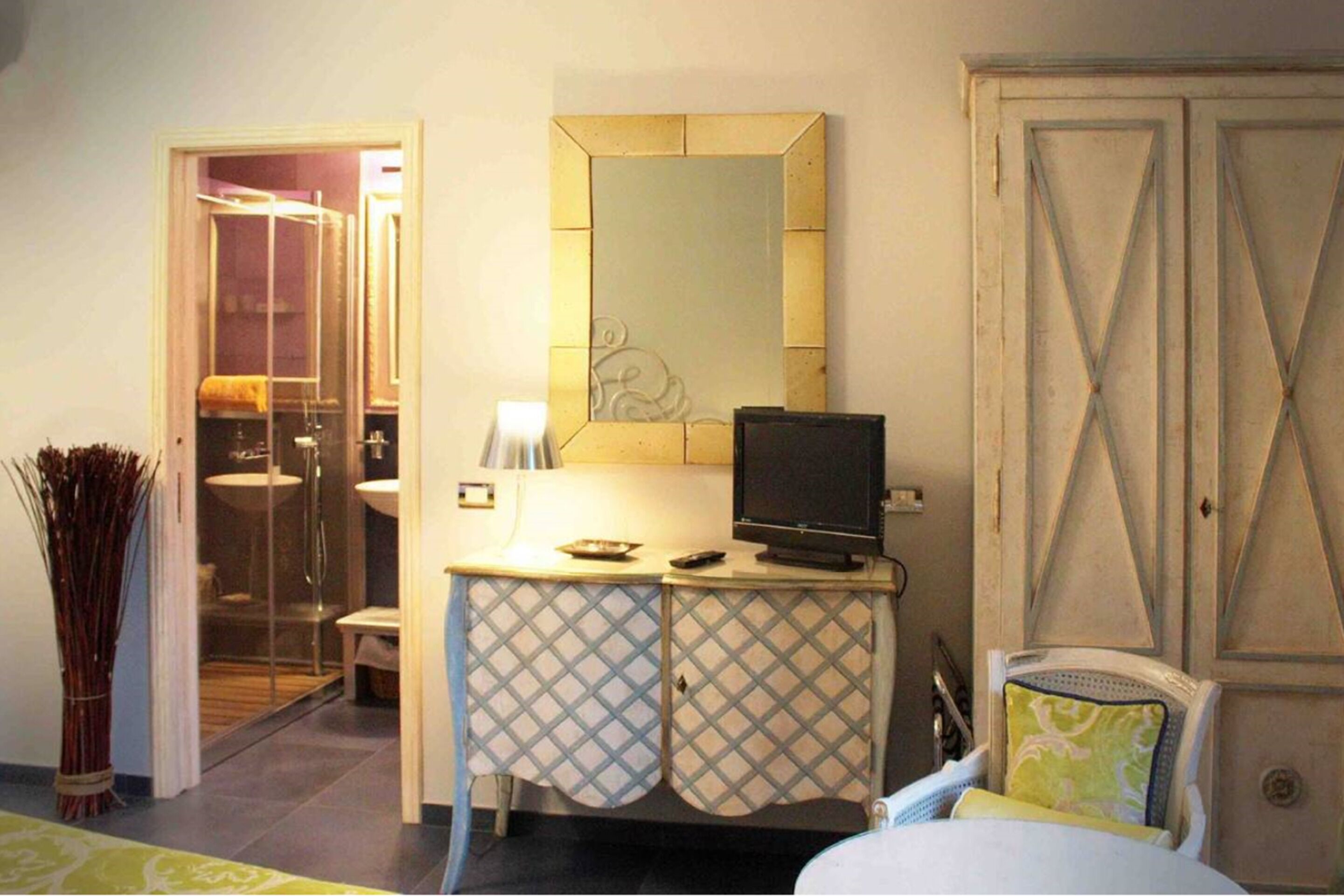 A hotel room with a bed, a desk with a television, a mirror, and a wardrobe.