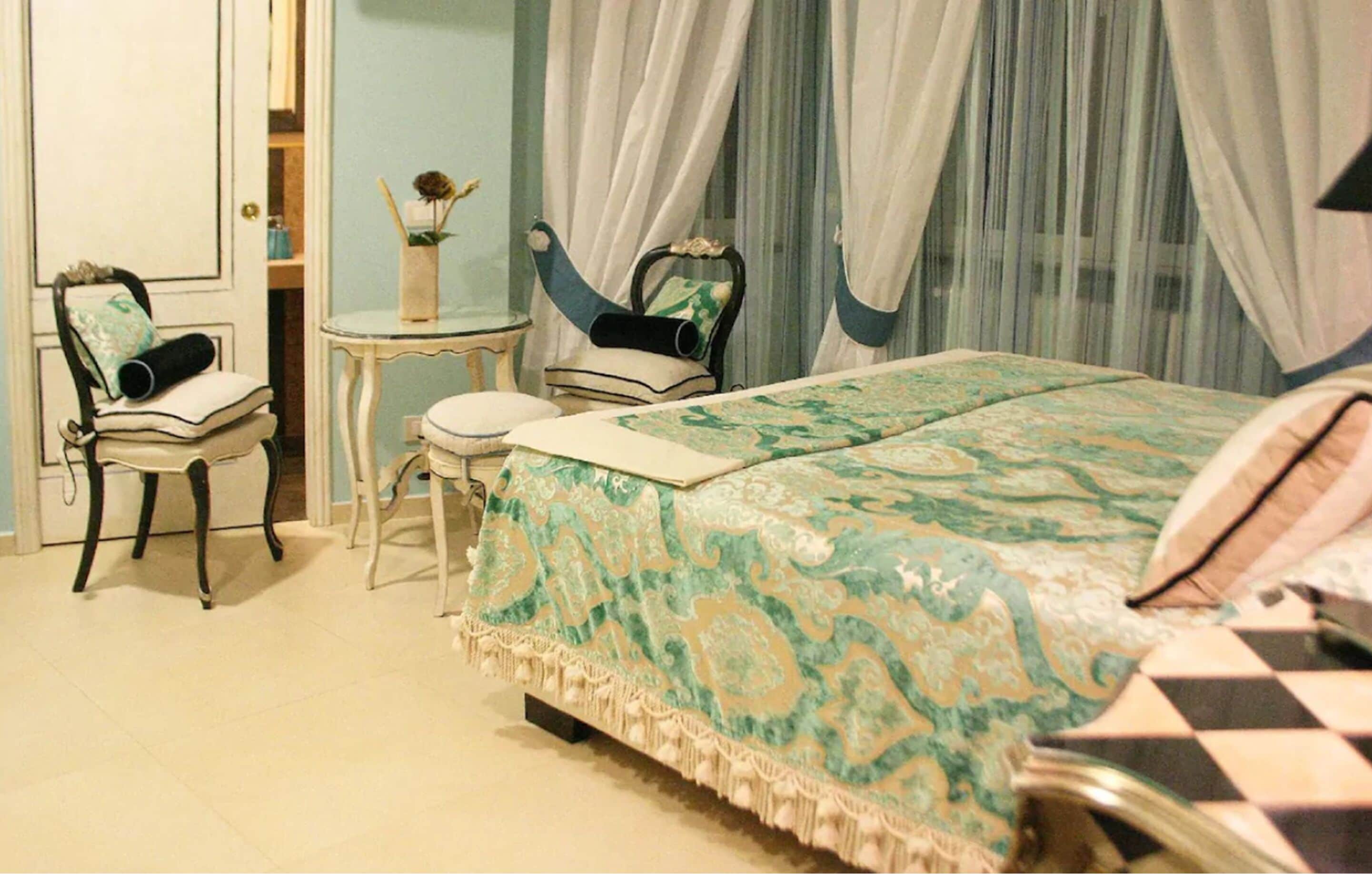 Un dormitorio con cama, dos sillones, una mesita y un espejo.
