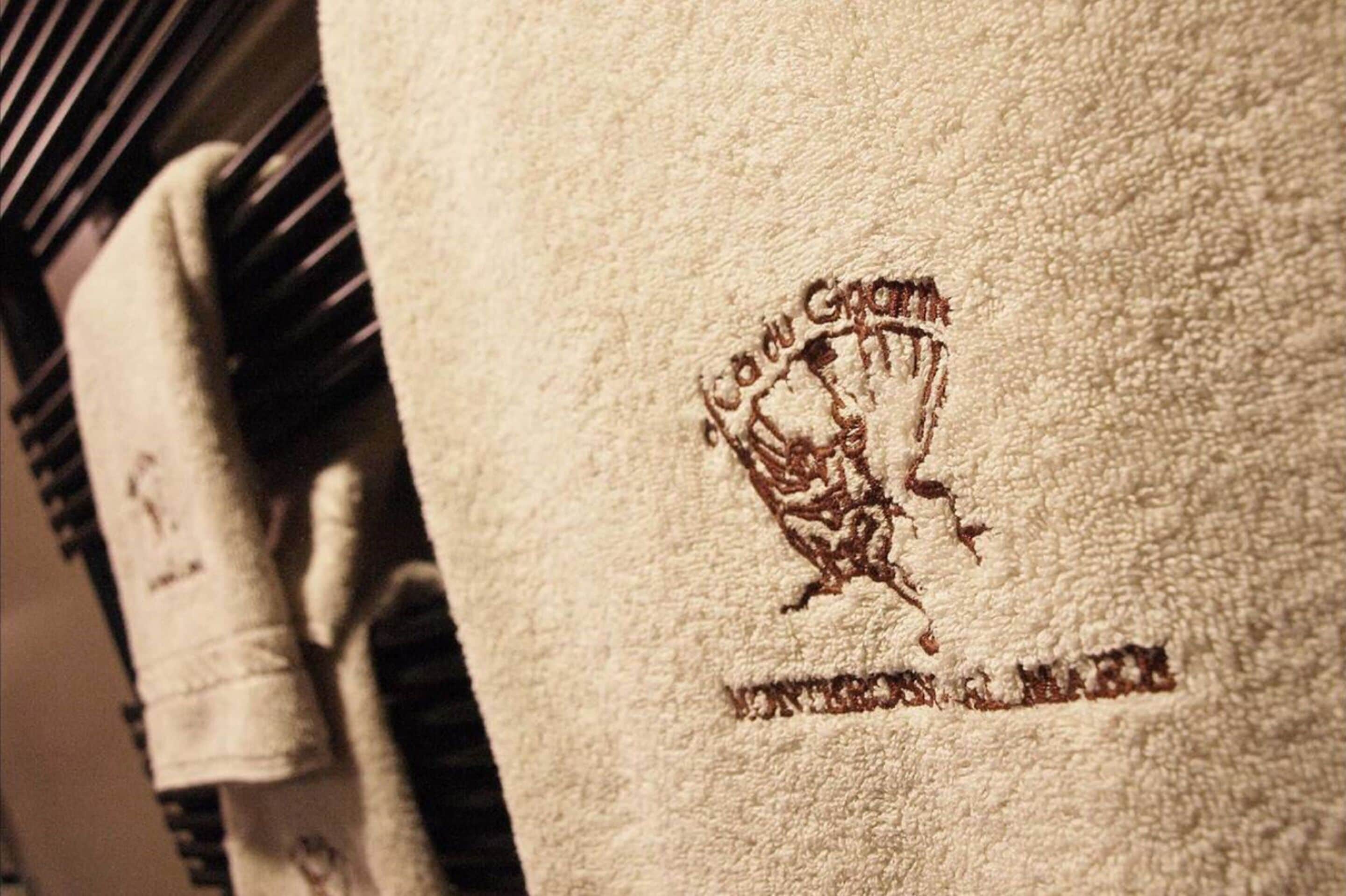 Una toalla con bordado de texto y logotipo, colgada en un perchero.
