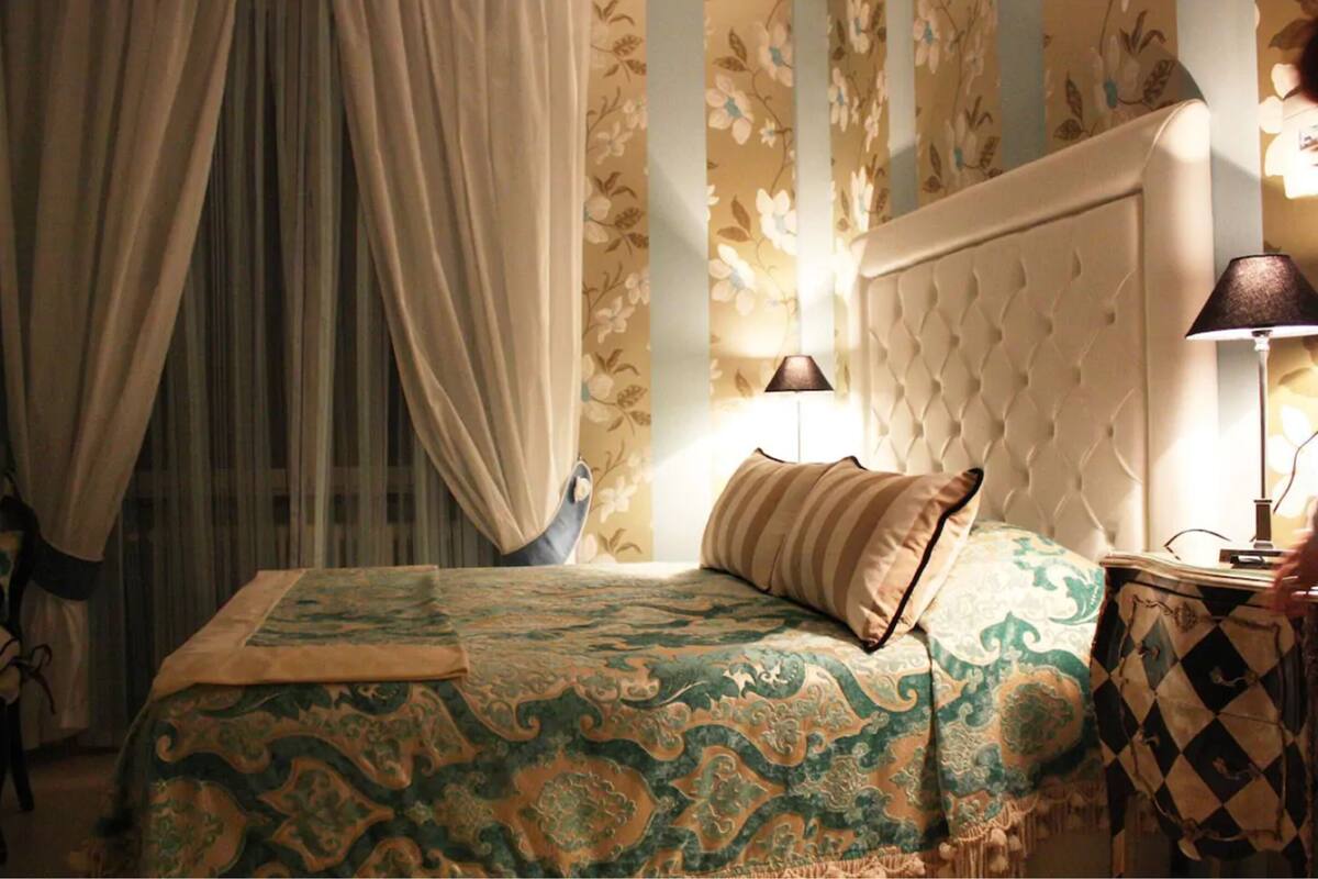 A bedroom with a bed, curtains, a nightstand, and a lamp.