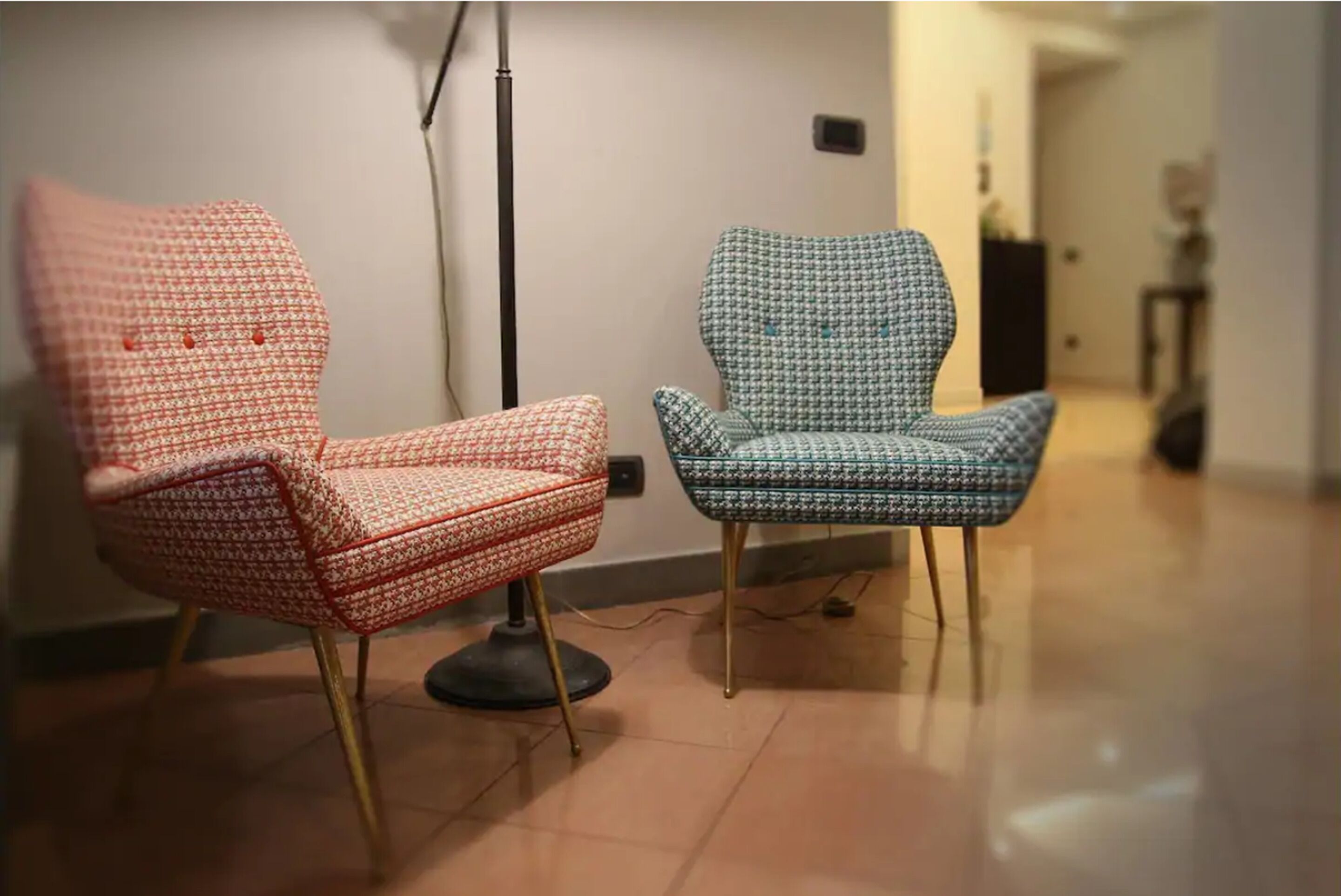 Two patterned chairs in a room with a tiled floor and a lamp in the background.
