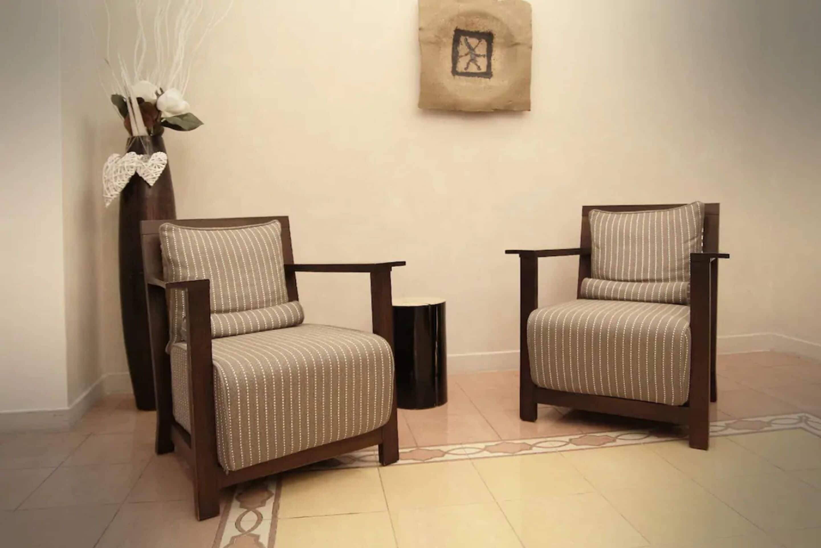 Two upholstered chairs with wooden frames and a decorative vase with branches and a bow on a table.