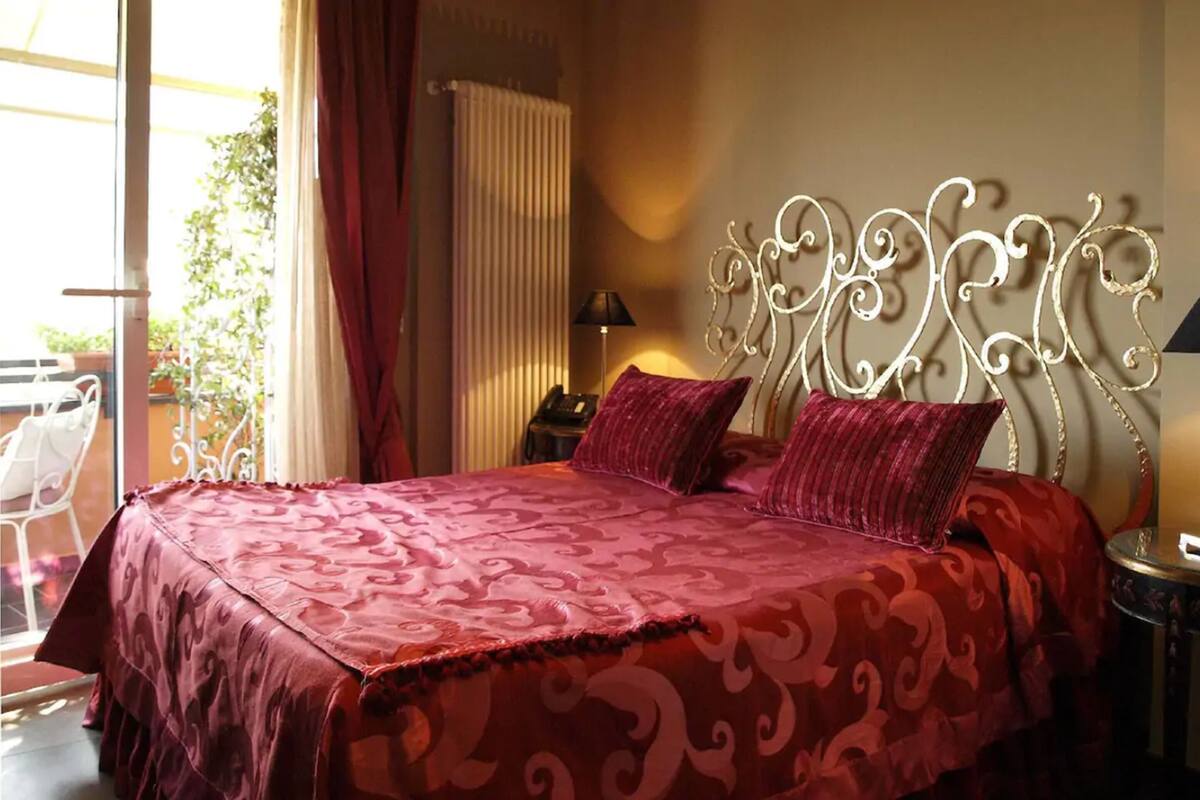 A bedroom with a large bed, a decorative headboard, and a view of the outdoors.