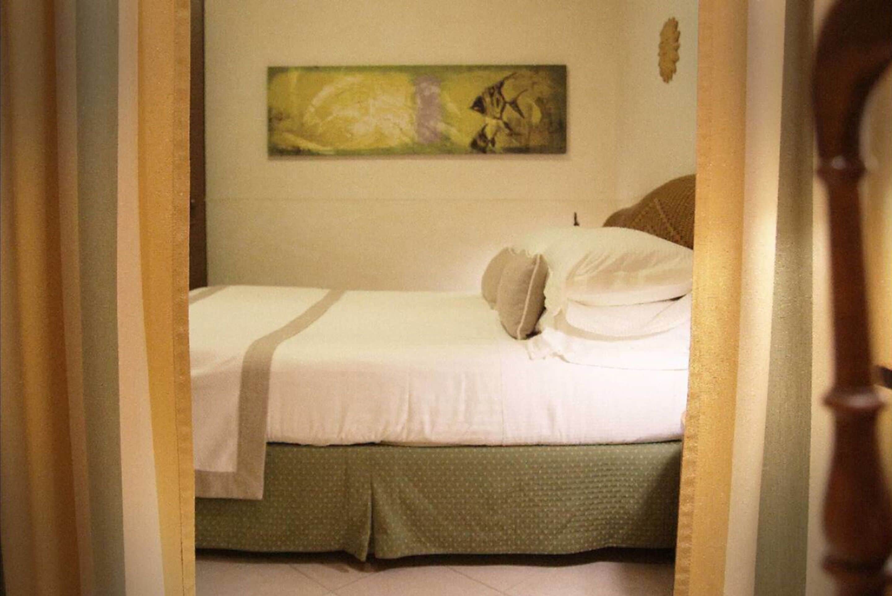 A neatly made bed with a green skirt, a white pillow, and a beige pillow.