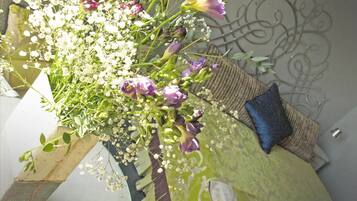 Um arranjo floral num canto do quarto, com uma almofada estampada e um ornamento metálico na parede.