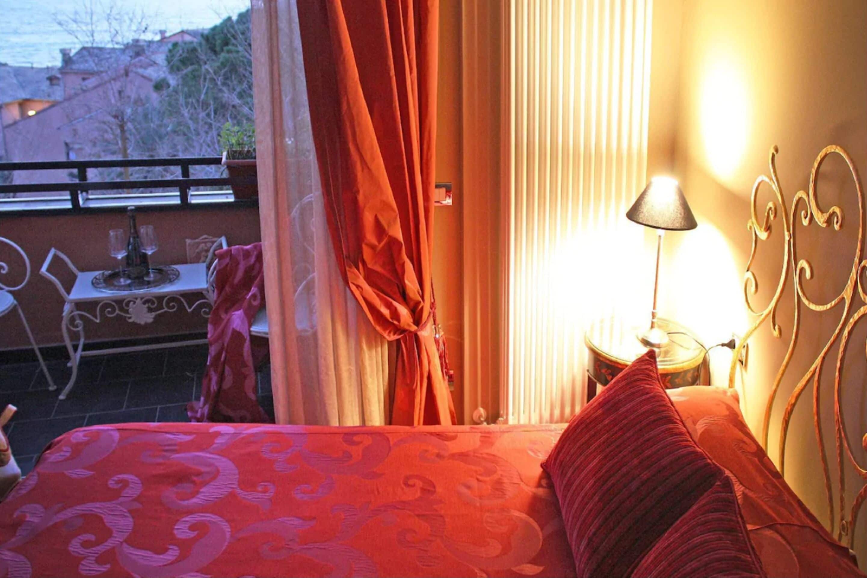A hotel room with a bed, a table with two chairs, a lamp, and a view of the outside.